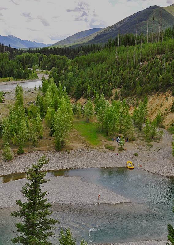 An aerial view of a river bed where a yellow raft is parked, and a man is standing on a bank