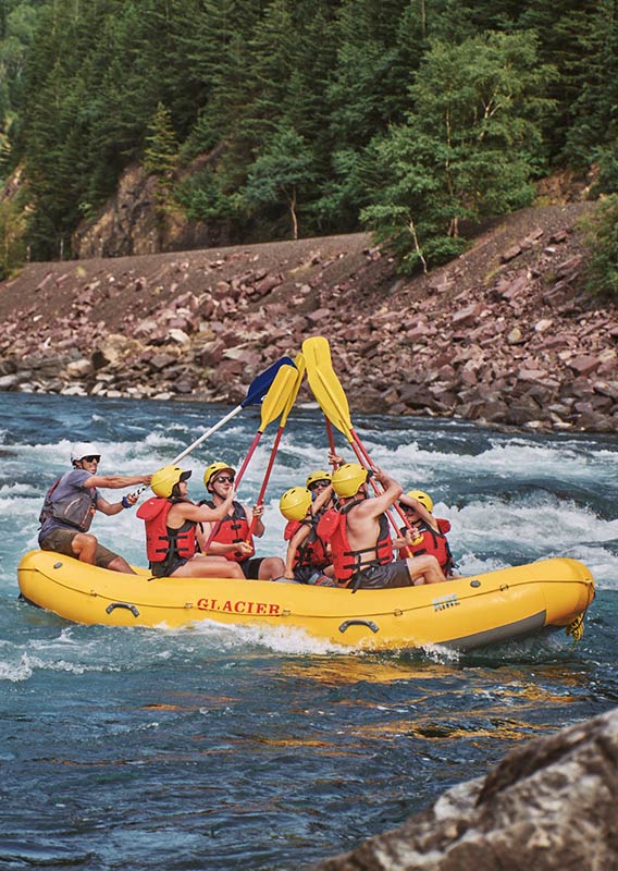 A group of rafters in a boat lift their paddles and touch the tips