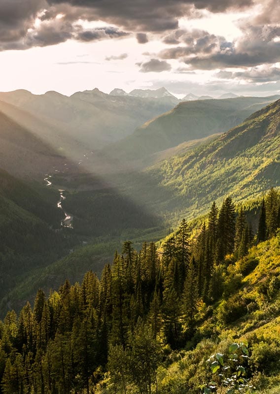 The sun shines over a wide, tree-covered valley