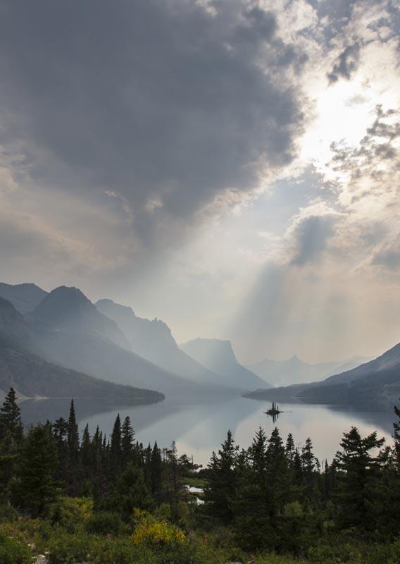 An island in mist on a lake surrounded by towering mountains