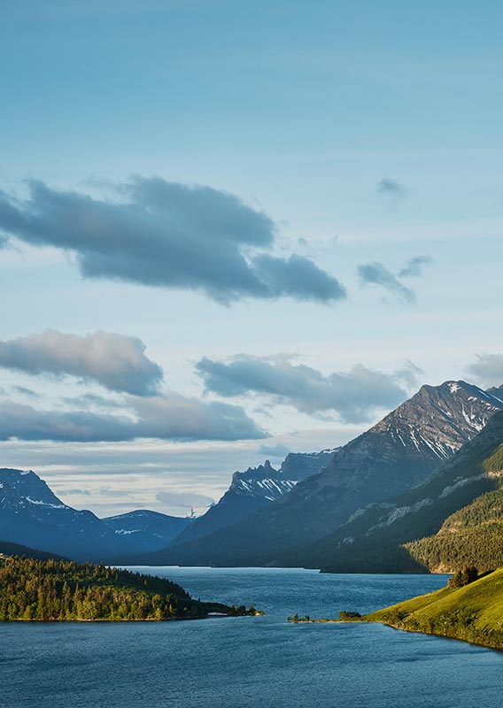 A large blue lake between tree-covered and snow-topped mountains.