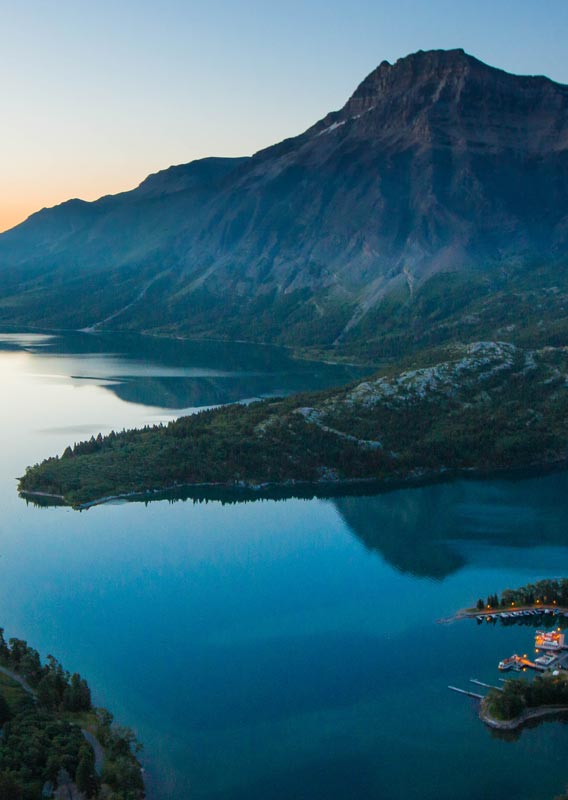 An aerial view of a small town alongside a long blue lake between mountains.