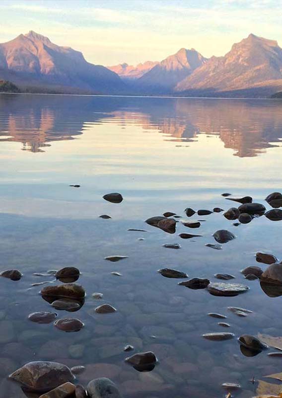 A view across a clear lake towards mountain peaks.