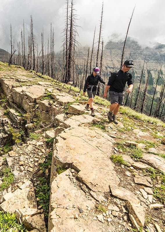 Two hikers walk along a ridge with a dramatic cliff drop on one side of the path