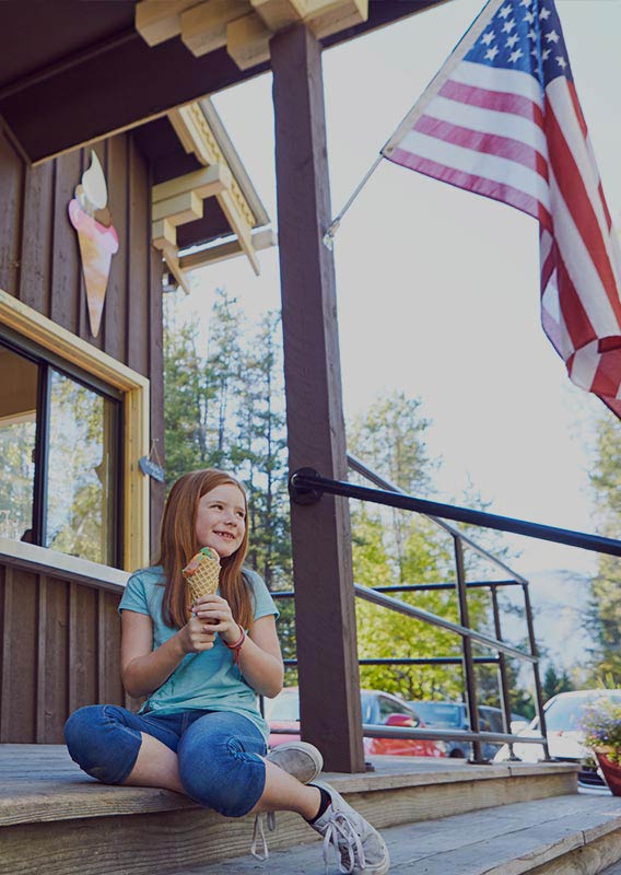 A smiling child sits on the exterior ice cream shop steps with an ice cream cone