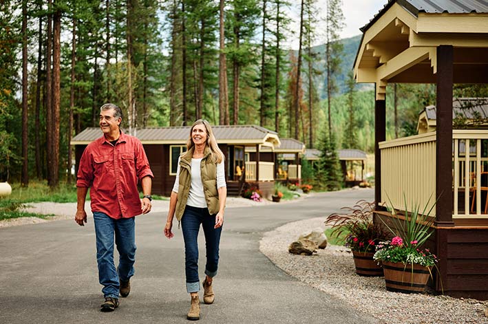 Two people walk on a small road between wooden cabins.