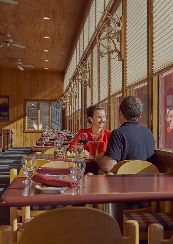 A couple sit at a windowside dining table, with views of mountains outside