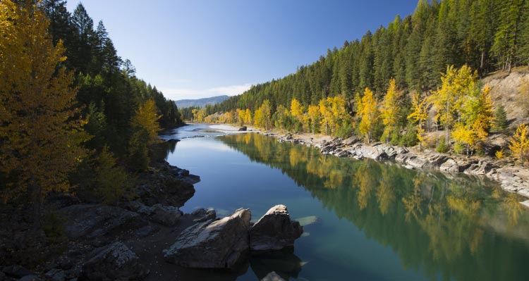 A river flows between shorelines covered by green and yellow trees.