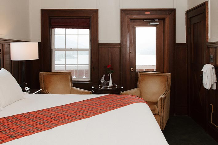 A hotel room bed and chairs by a door and window.