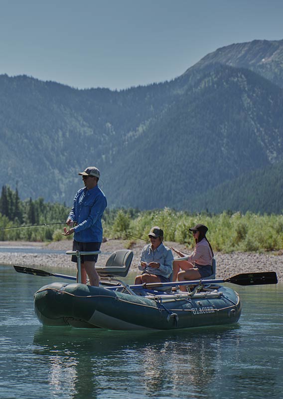 A man in blue stands and reels in a line on a boat with two other sitting in the back.