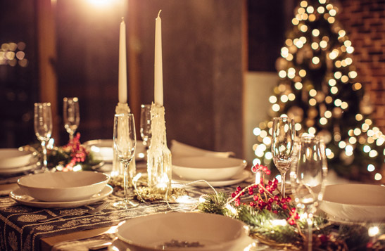 A holiday table setting with a lit up Christmas tree in the background