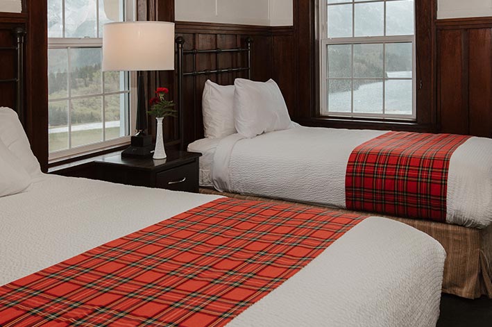 Two hotel beds in a corner hotel room with windows overlooking a lake.