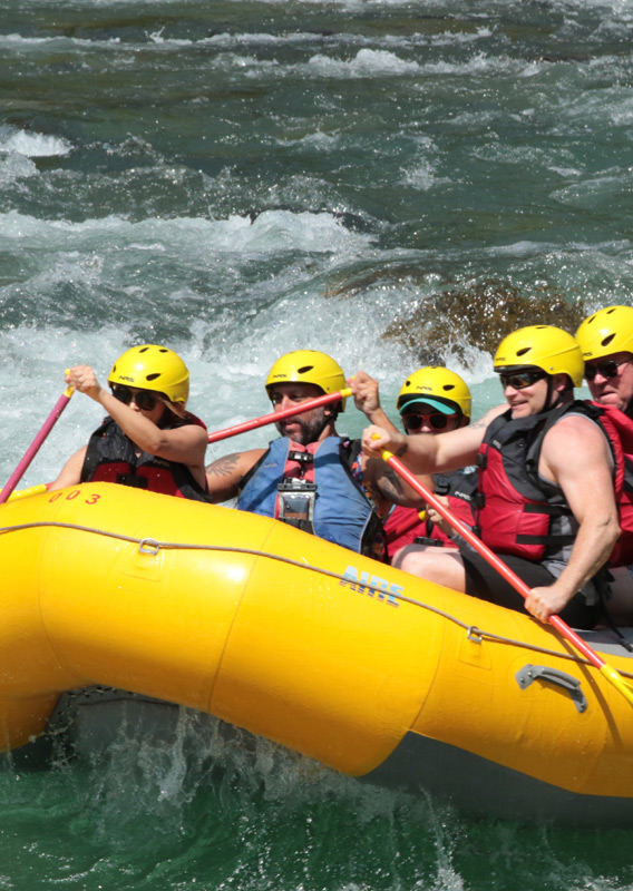 A rafting group smilling and having fun rowing through river rapids.