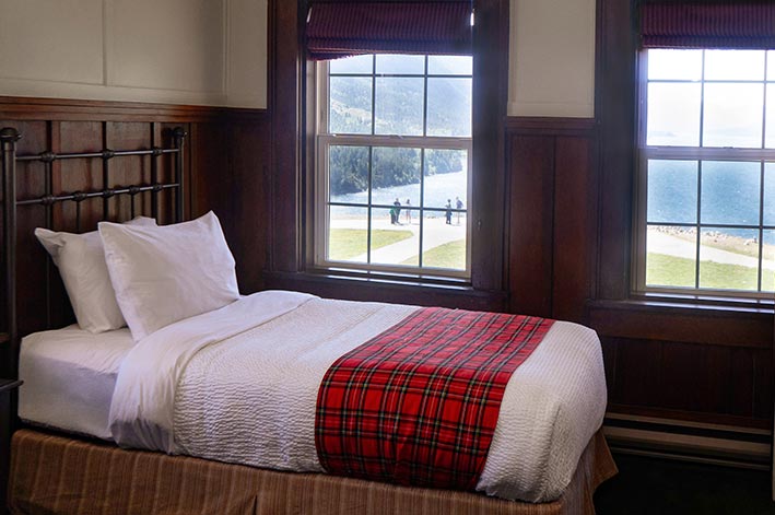 A hotel bed next to two windows.