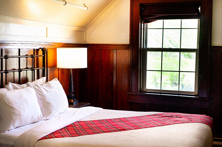 A hotel bed near a window overlooking a forest.