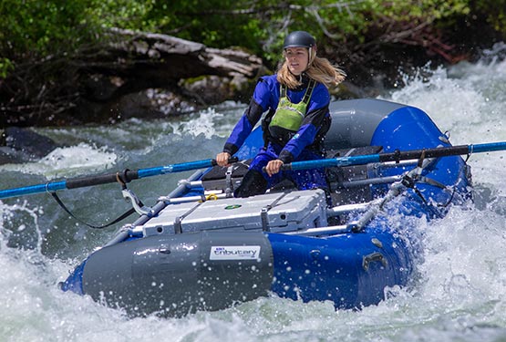 A rafter takes a blue boat through whitewater rapids.