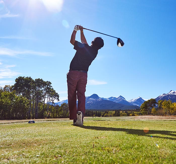 A golfer swings his driver at a green.