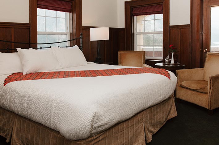 A bed and chairs next to the corner windows of a hotel room.