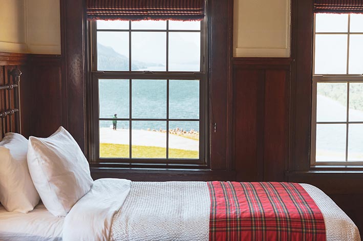 A hotel bed next to two windows.