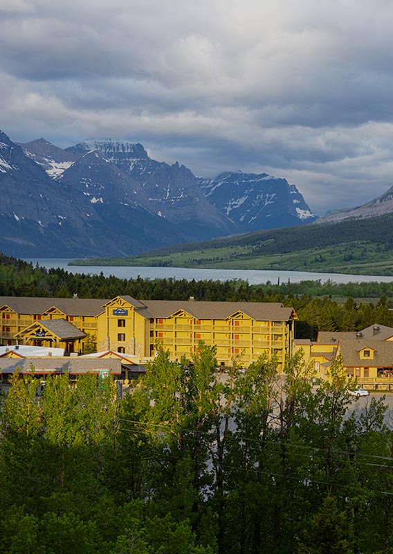 A view of St. Mary Village below mountains and a wide blue lake.