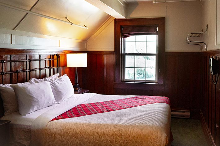A hotel bed near a window overlooking a forest.